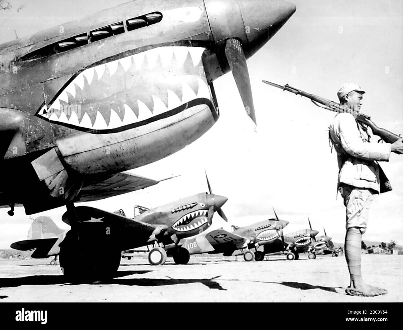 China: A Chinese KMT soldier guards a line of American P-40 fighter planes, painted with the shark-face emblem of the `Flying Tigers,' SW China, 1942.  Flying Tigers was the popular name of the 1st American Volunteer Group (AVG) of the Chinese Air Force in 1941-1942. The pilots were United States Army (USAAF), Navy (USN), and Marine Corps (USMC) personnel, recruited under Presidential sanction and commanded by Claire Lee Chennault; the ground crew and headquarters staff were likewise mostly recruited from the U.S. military, along with some civilians. Stock Photo